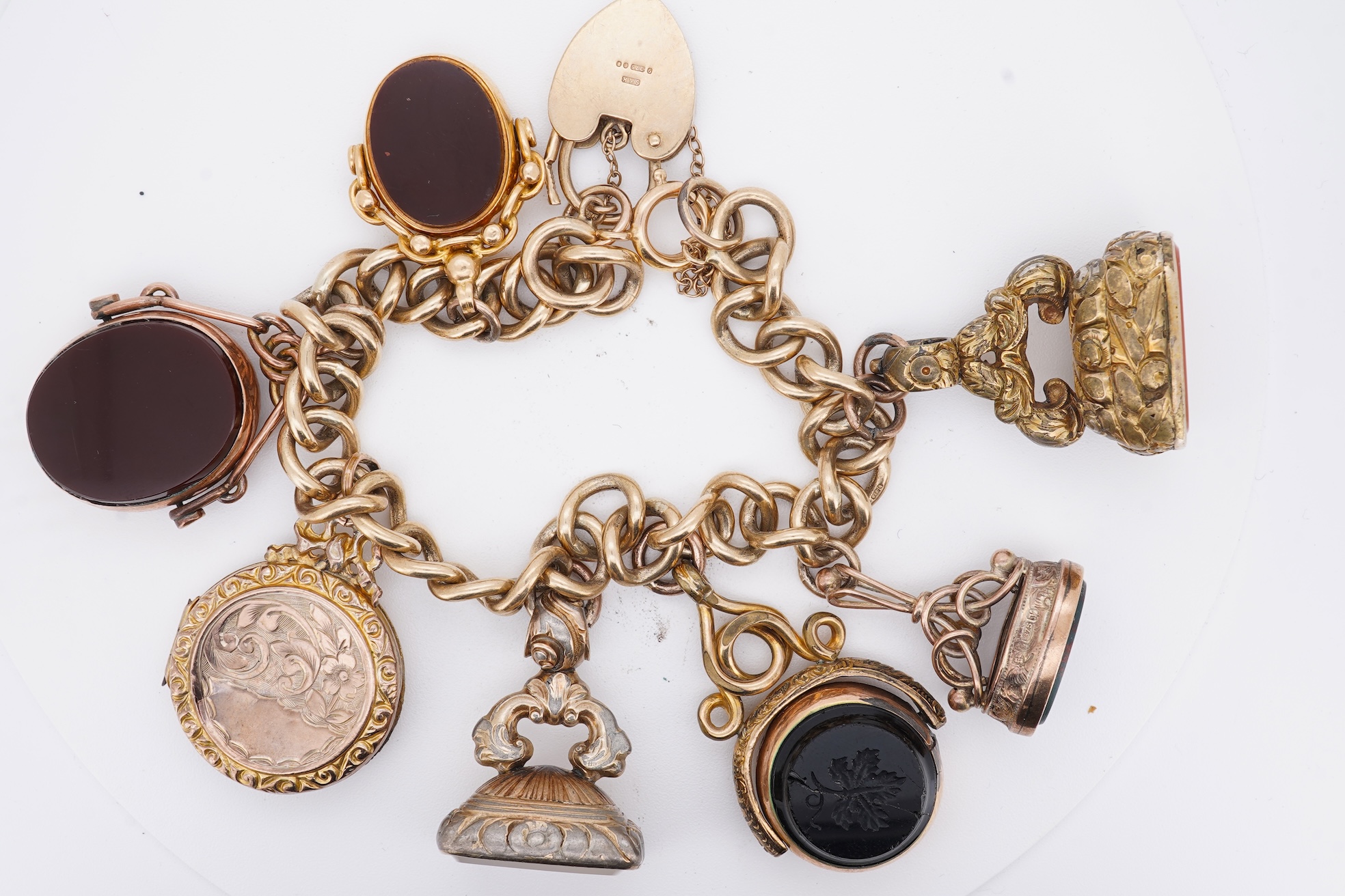 A 1970's 9ct gold curb link charm bracelet, with 9ct gold heart shaped clasp, hung with seven assorted gold or gilt metal mounted charms including six chalcedony set fob seals, gross weight 73 grams.
